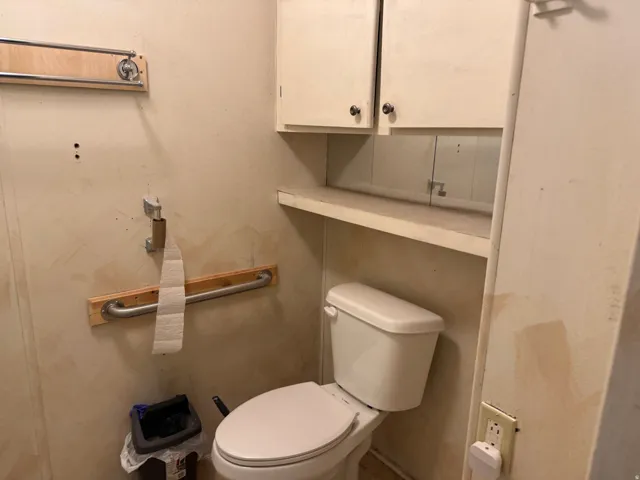 White toilet with a built-in shelf, two upper wall cabinets, and metal grab bars