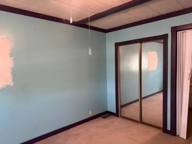 Room featuring light blue walls with dark trim, wall-to-wall carpeting, and a mirrored closet with sliding doors