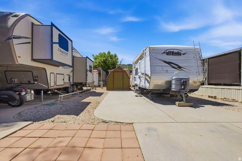 Paved concrete and paver stone surfaces, gravel areas, and a small storage shed