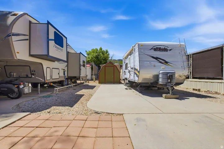 Paved concrete and paver stone surfaces, gravel areas, and a small storage shed