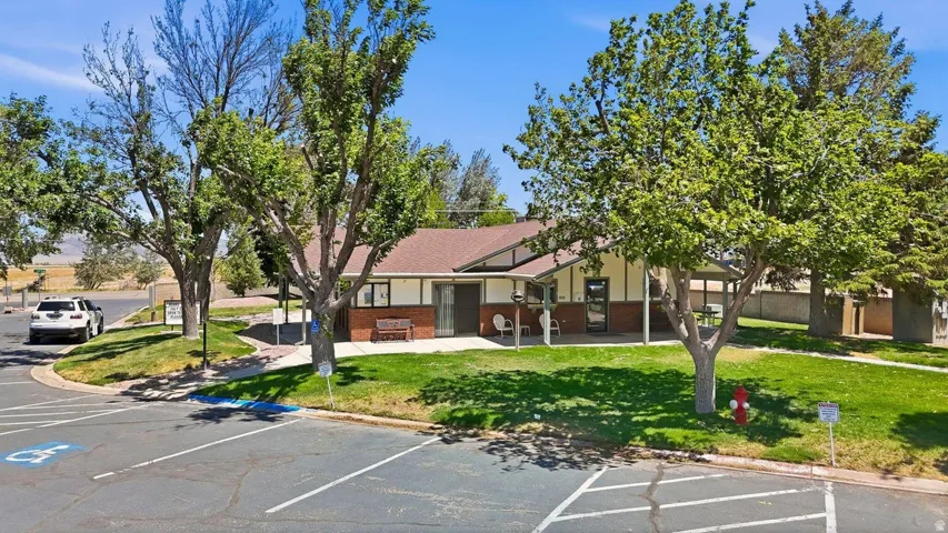 Community building featuring a hip roof, brick and siding exterior, covered patio, and mature trees