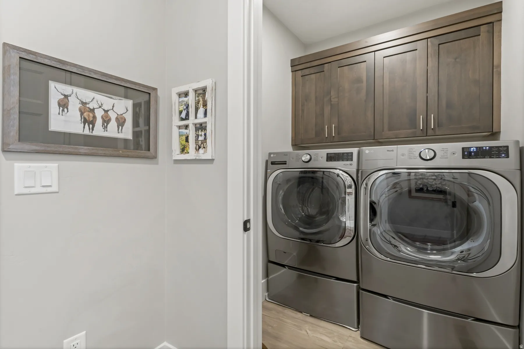 Dedicated laundry area featuring wood-finish cabinetry, light gray walls, and wood-finish flooring