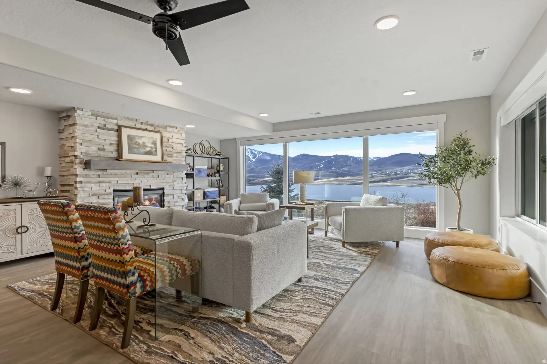 Spacious living area featuring a stacked stone fireplace with a substantial wood mantle, light wood-finish flooring, recessed lighting, and a prominent ceiling fan