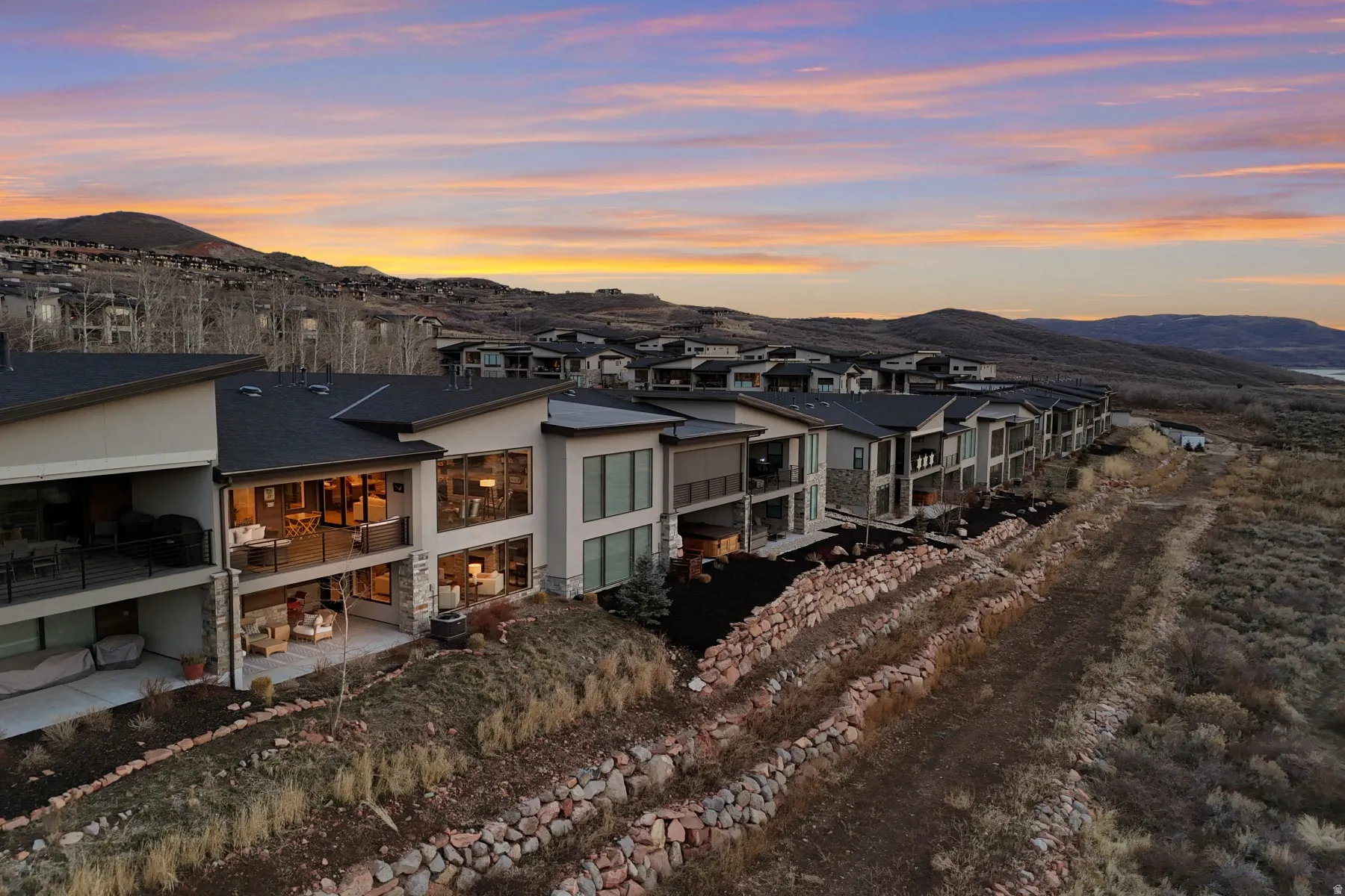 Contemporary architectural design featuring expansive glass walls, multiple outdoor balconies, stone and stucco exterior finishes, and a dark shingle roof