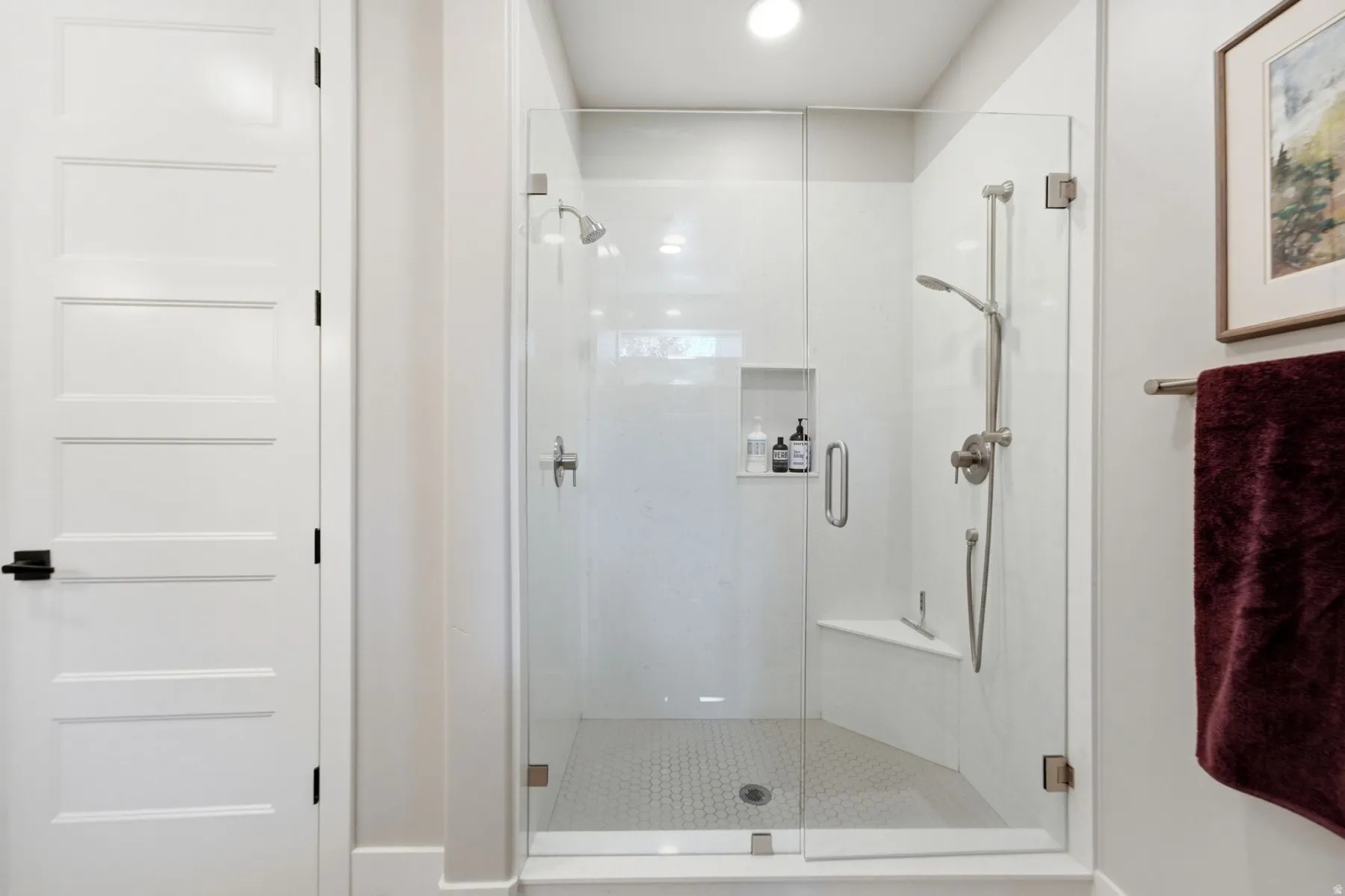 Glass-enclosed shower featuring a built-in bench, recessed niche, rain shower head, and a handheld shower wand