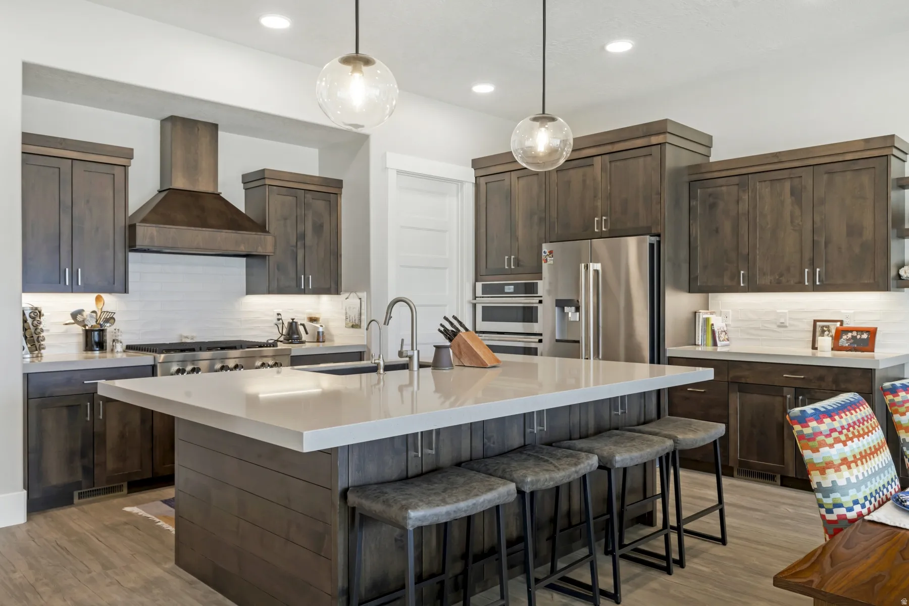 Expansive kitchen featuring a large central island with seating, dark wood cabinetry, stainless steel appliances, a paneled range hood, and wood-finish flooring