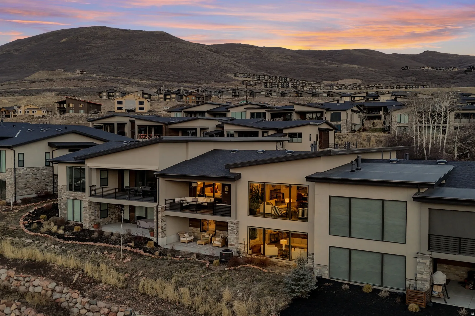Contemporary multi-level residence featuring expansive windows, private balconies, stone accents, flat rooflines, and a terraced landscape