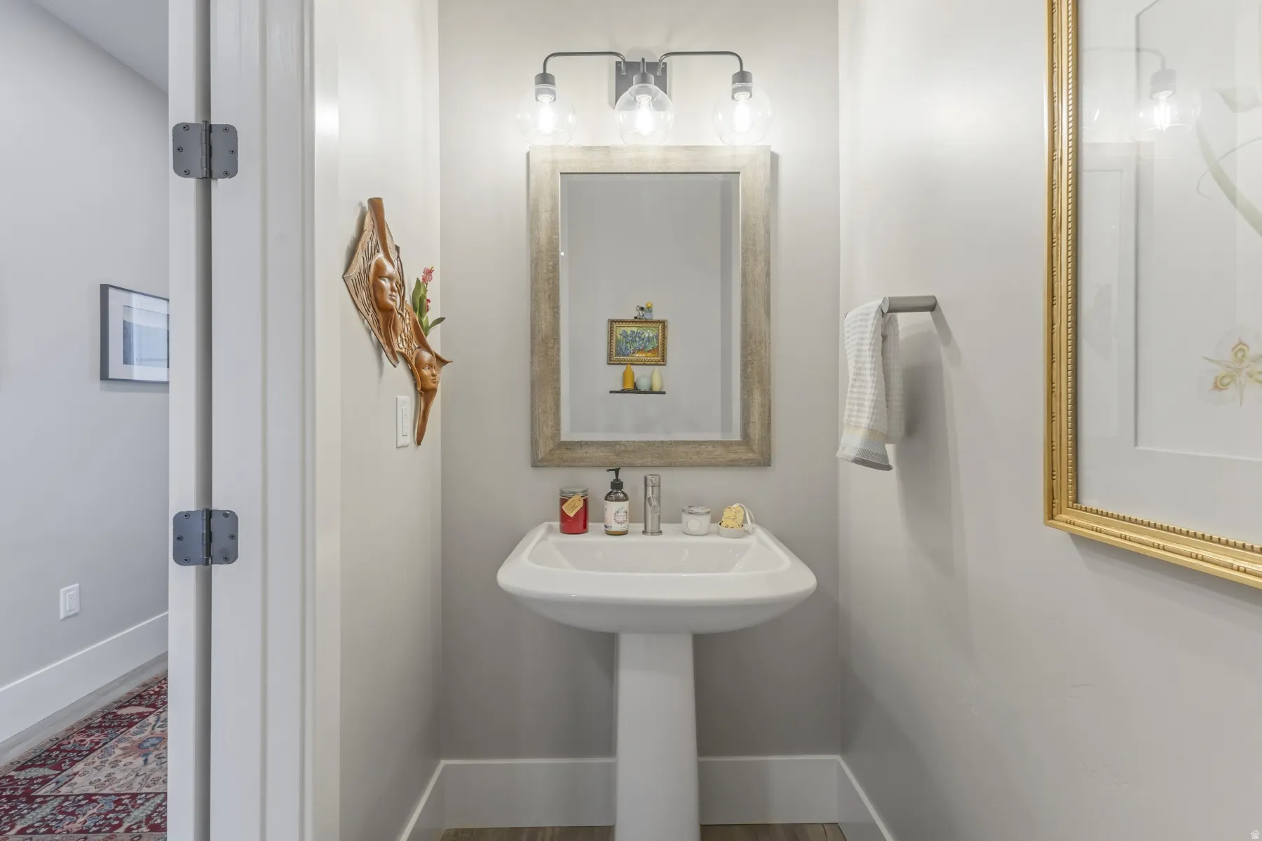 Pedestal sink with chrome faucet, framed mirror, and three-bulb vanity light fixture