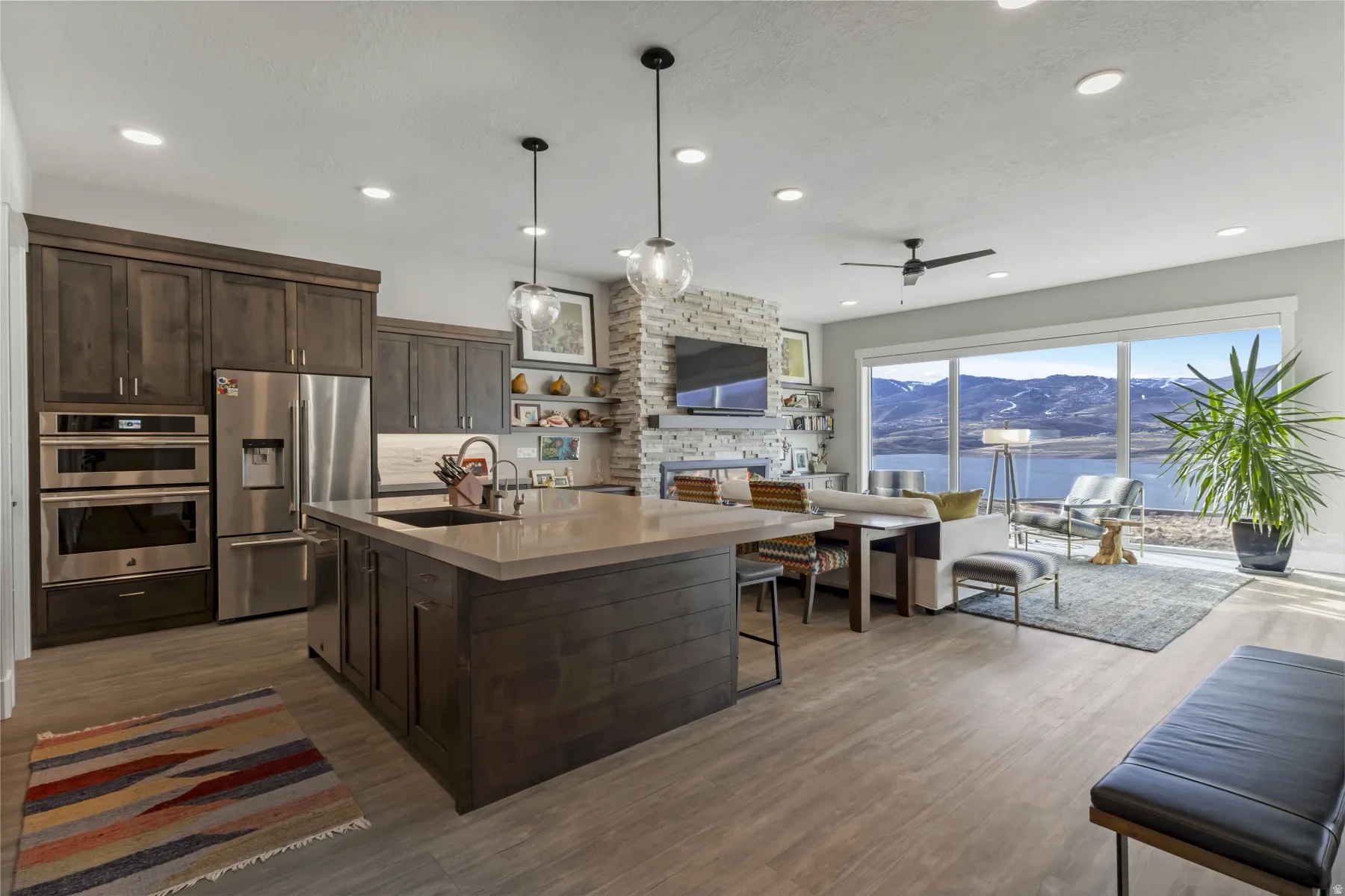 Open concept living area featuring wood-finish flooring, a kitchen island with seating, dark wood cabinetry, stainless steel appliances, and a stone accent wall
