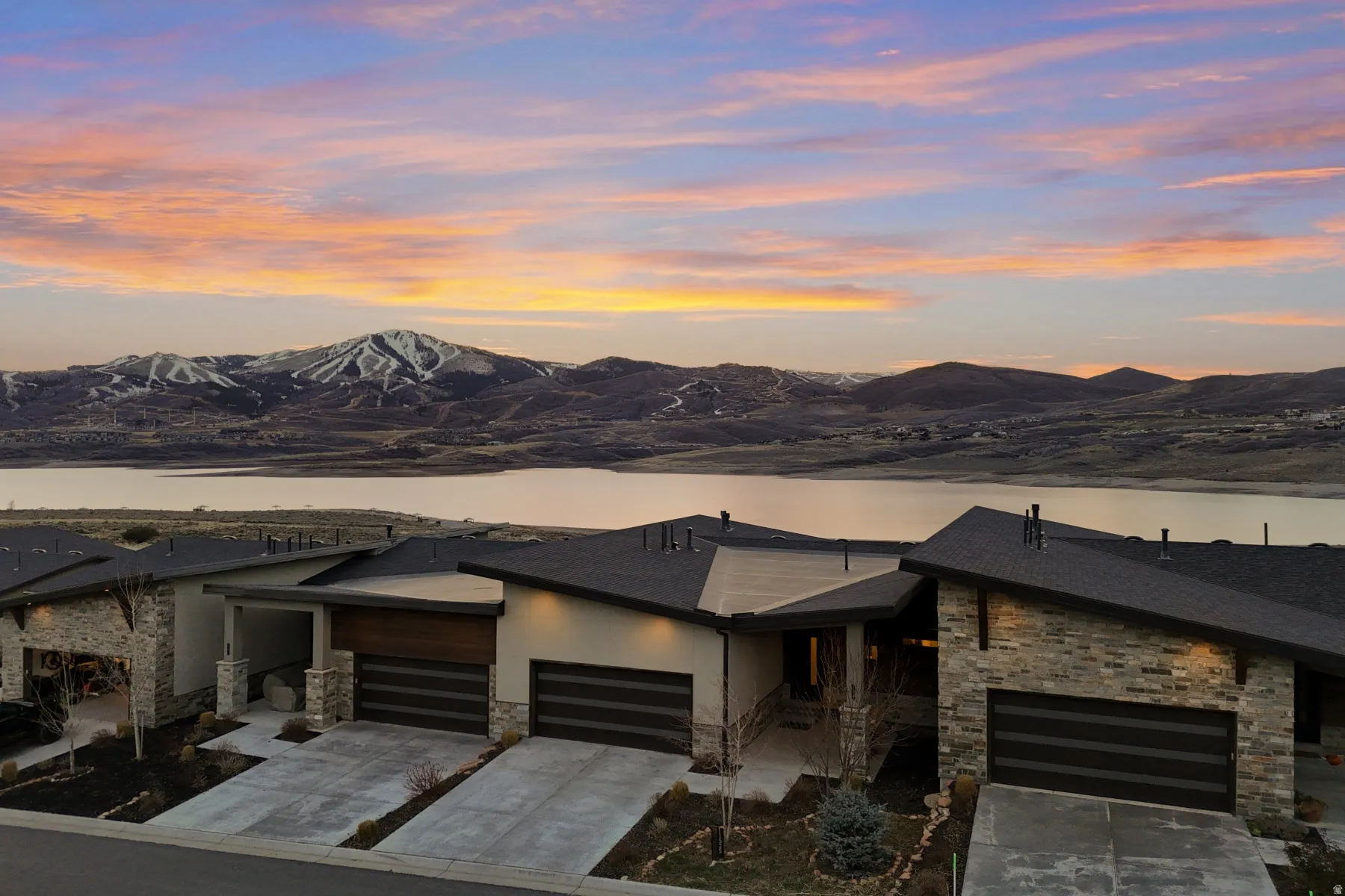 Modern architectural homes featuring stone and horizontal wood-finish accents, individual garages, and concrete driveways