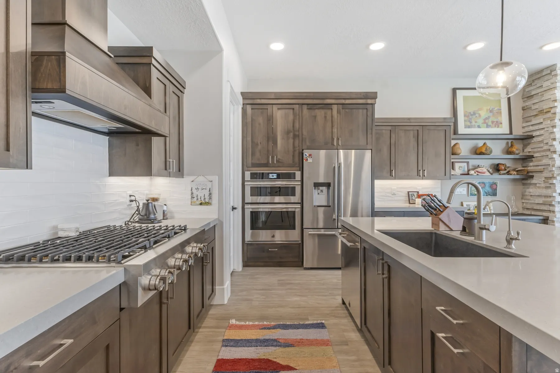 Gourmet kitchen featuring a built-in gas range with vent hood, stainless steel appliances, a large center island with an undermount sink, and extensive cabinetry