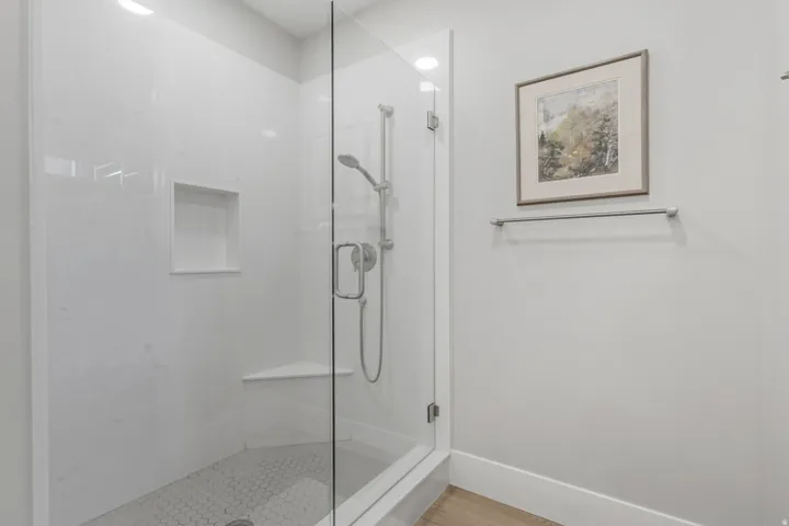 Glass-enclosed shower featuring white wall panels, a built-in niche, and a corner bench