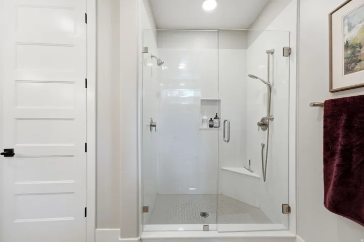 Glass-enclosed shower featuring a built-in bench, recessed niche, rain shower head, and a handheld shower wand