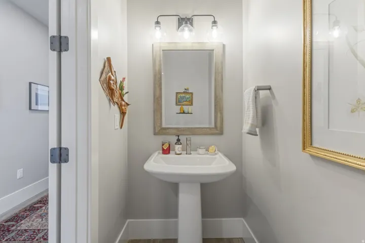 Pedestal sink with chrome faucet, framed mirror, and three-bulb vanity light fixture