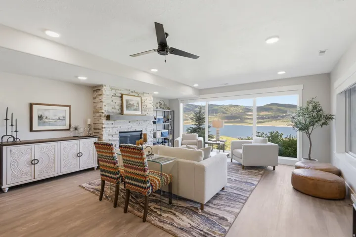 Spacious living area featuring large windows, a stone fireplace with a wood mantle, wood-finish flooring, recessed lighting, and a ceiling fan