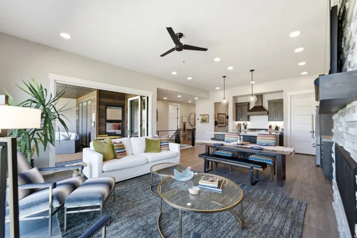 Open-concept living area with wood-finish flooring, a stacked stone fireplace, recessed lighting, and a contemporary ceiling fan