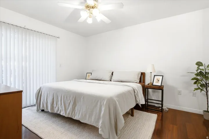 Bedroom featuring rich wood-finish flooring, white walls, and a ceiling fan with integrated lighting