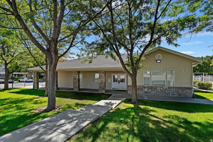 Clubhouse exterior featuring tan siding, stone veneer accents, a covered entry, and double white doors