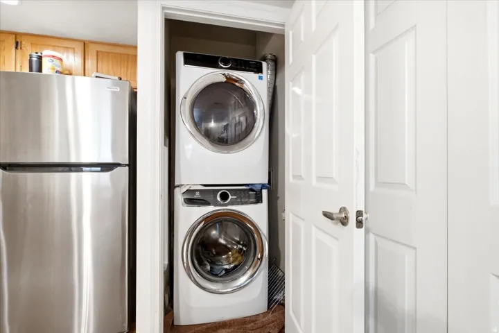 Dedicated laundry closet featuring a stackable washer and dryer, complemented by a stainless steel refrigerator and wood cabinetry