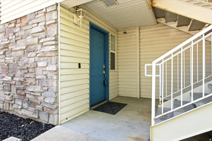 Entryway featuring a blue door, stone veneer accent, horizontal siding, concrete flooring, and an exterior staircase with metal railings