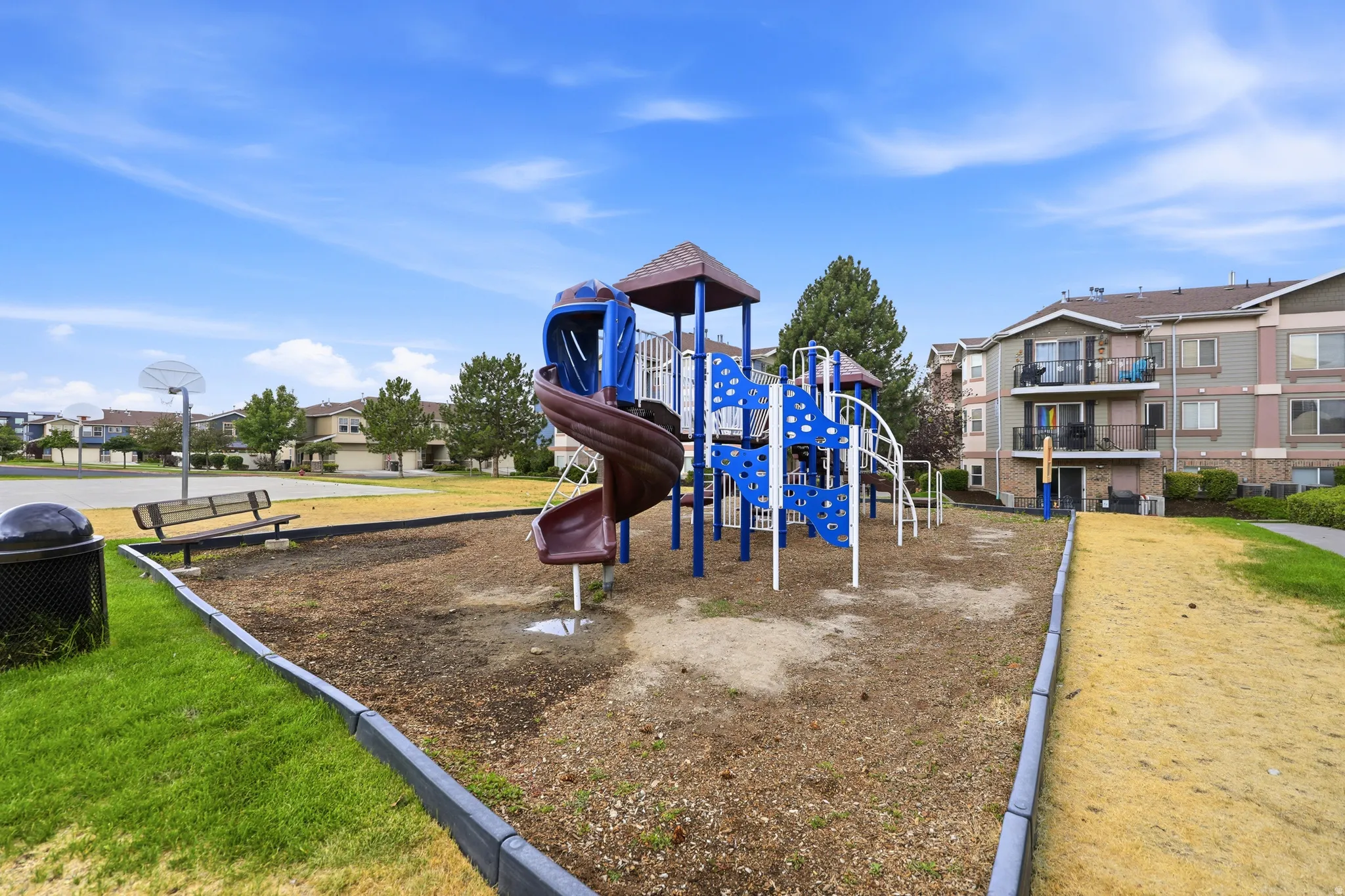 Community playground featuring a multi-level play structure with slides and climbing elements, surrounded by a wood chip surface