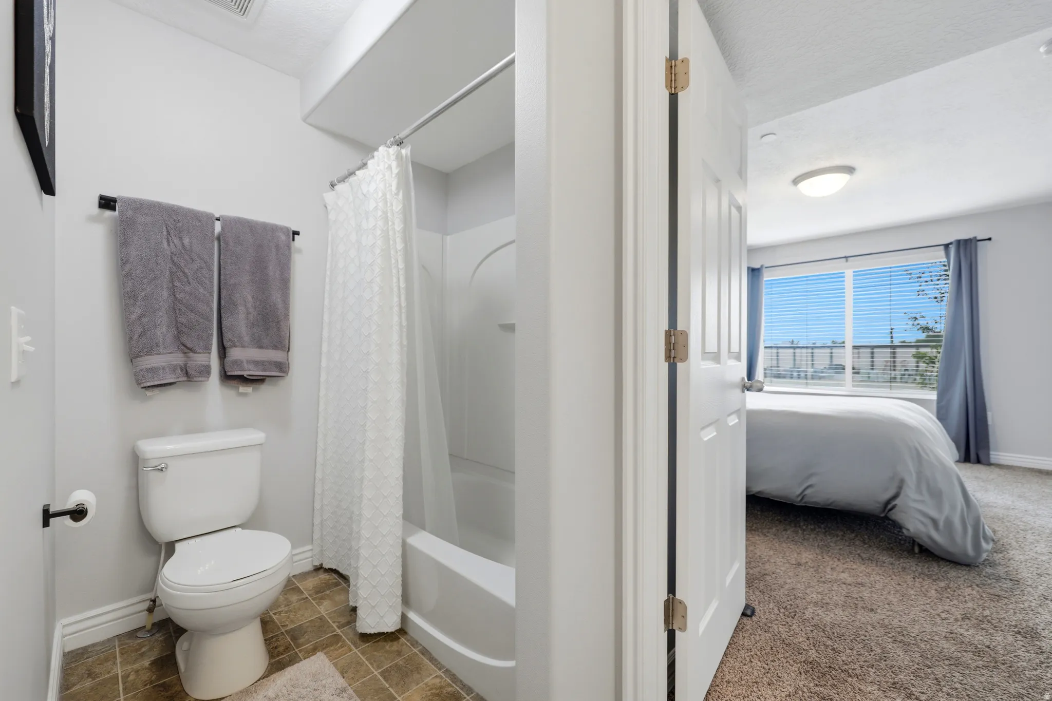 Bathroom featuring a white toilet, a shower-over-tub combination with a white shower curtain, and wood-finish tile flooring