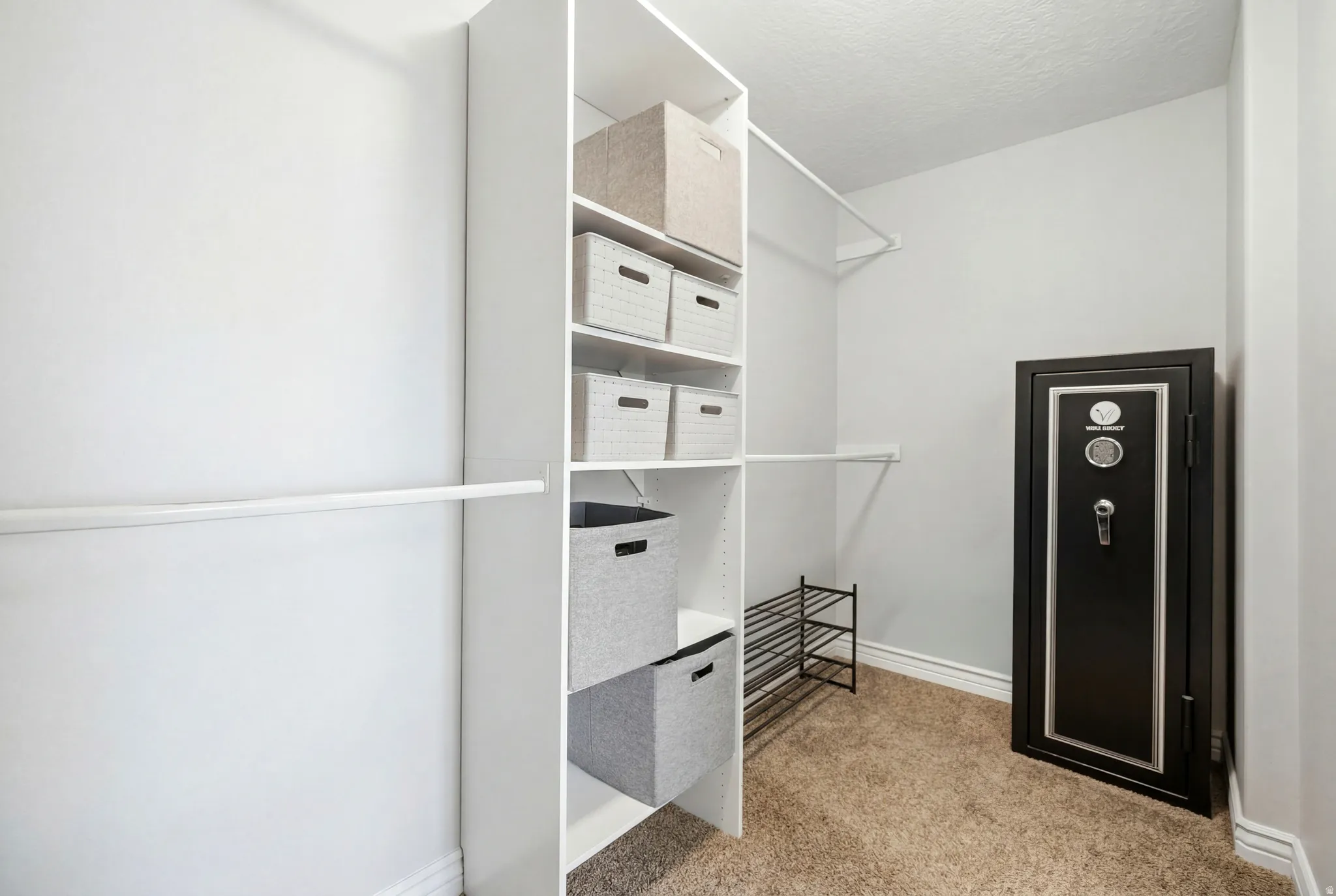Walk-in closet with white shelving units and hanging rods, complemented by light brown carpet flooring