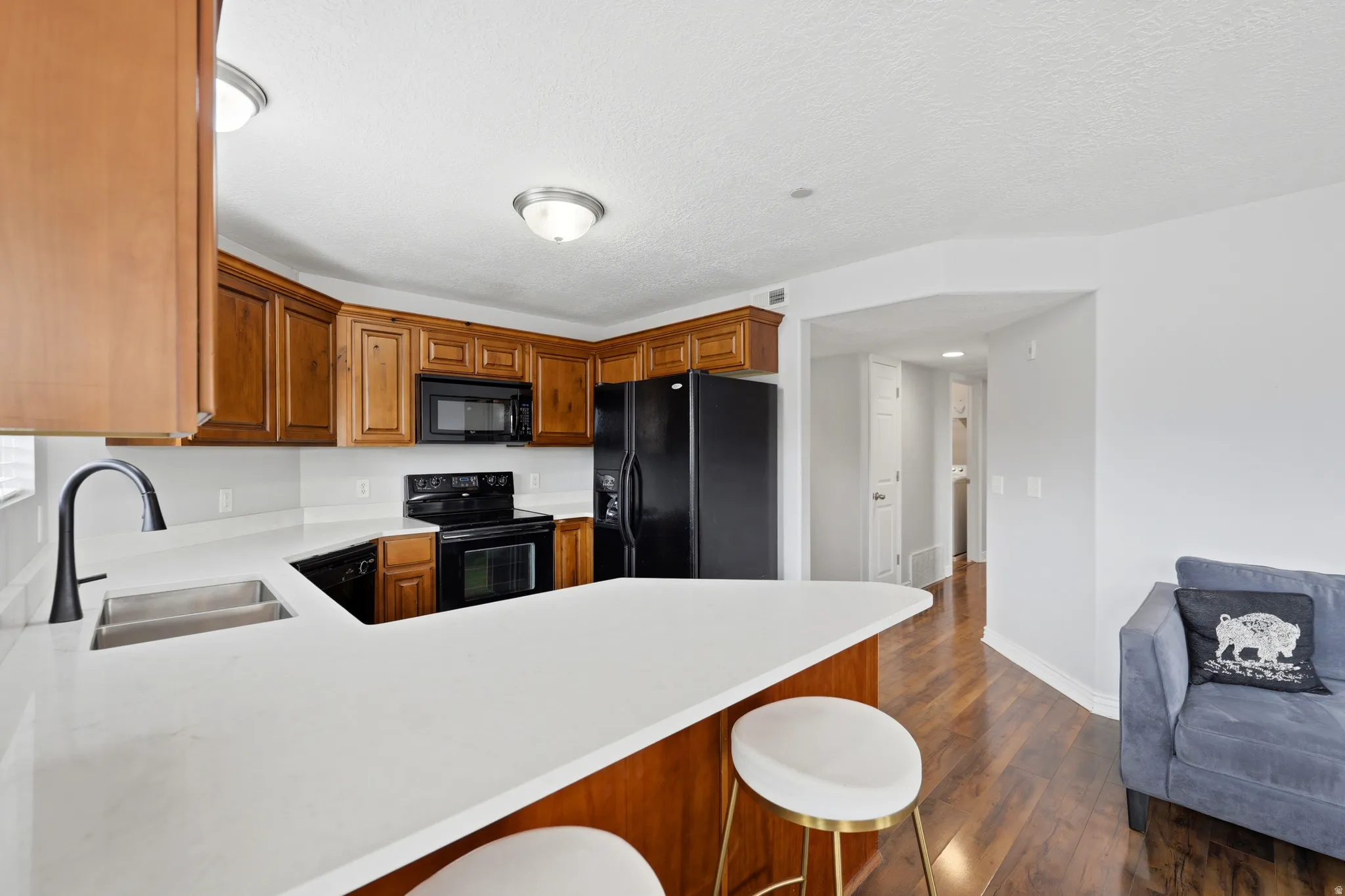 Kitchen featuring wood cabinetry, white countertops, a stainless steel double basin sink with a black faucet, and hardwood-style flooring