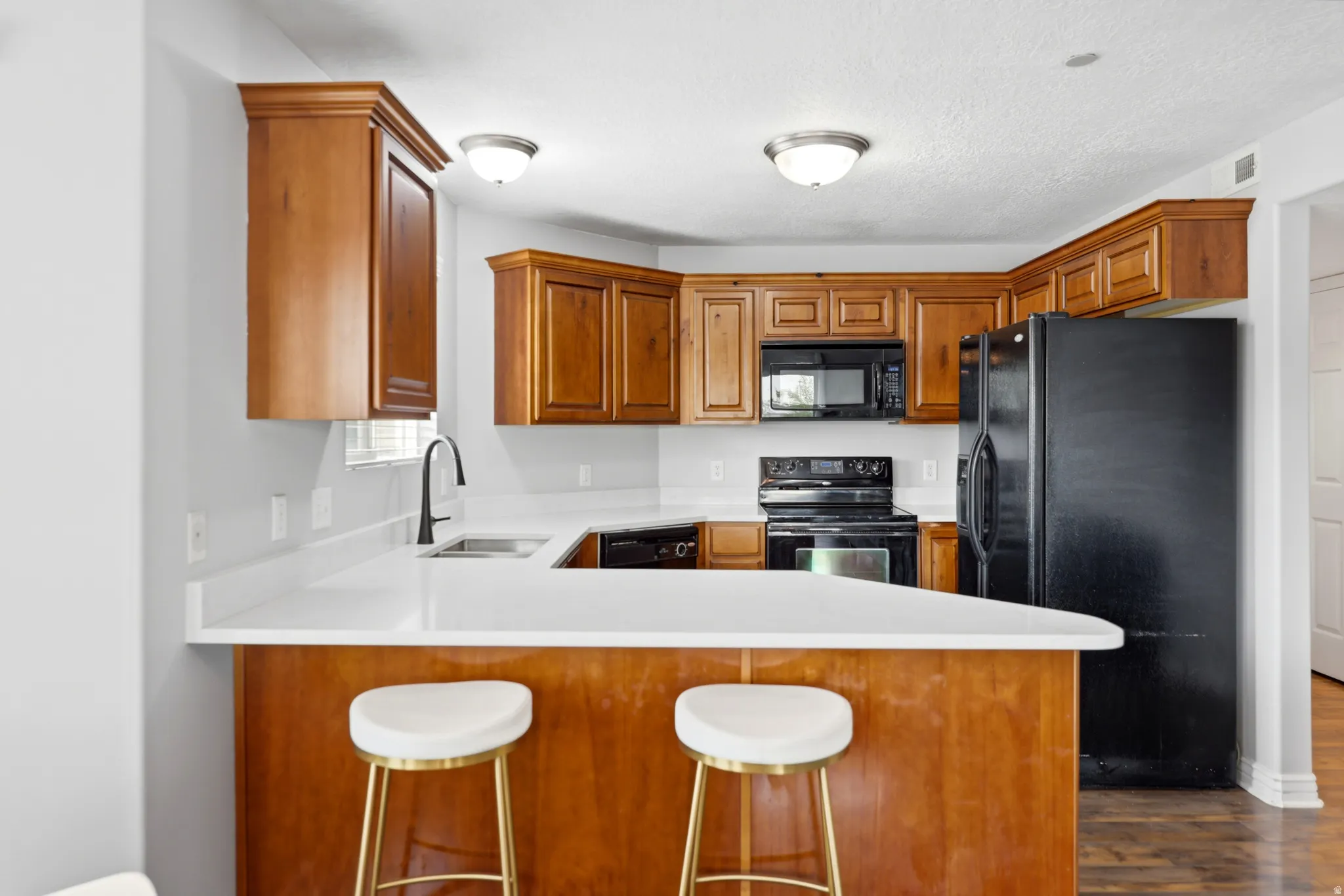Kitchen featuring wood cabinetry, white countertops, black appliances, and a breakfast bar with seating space
