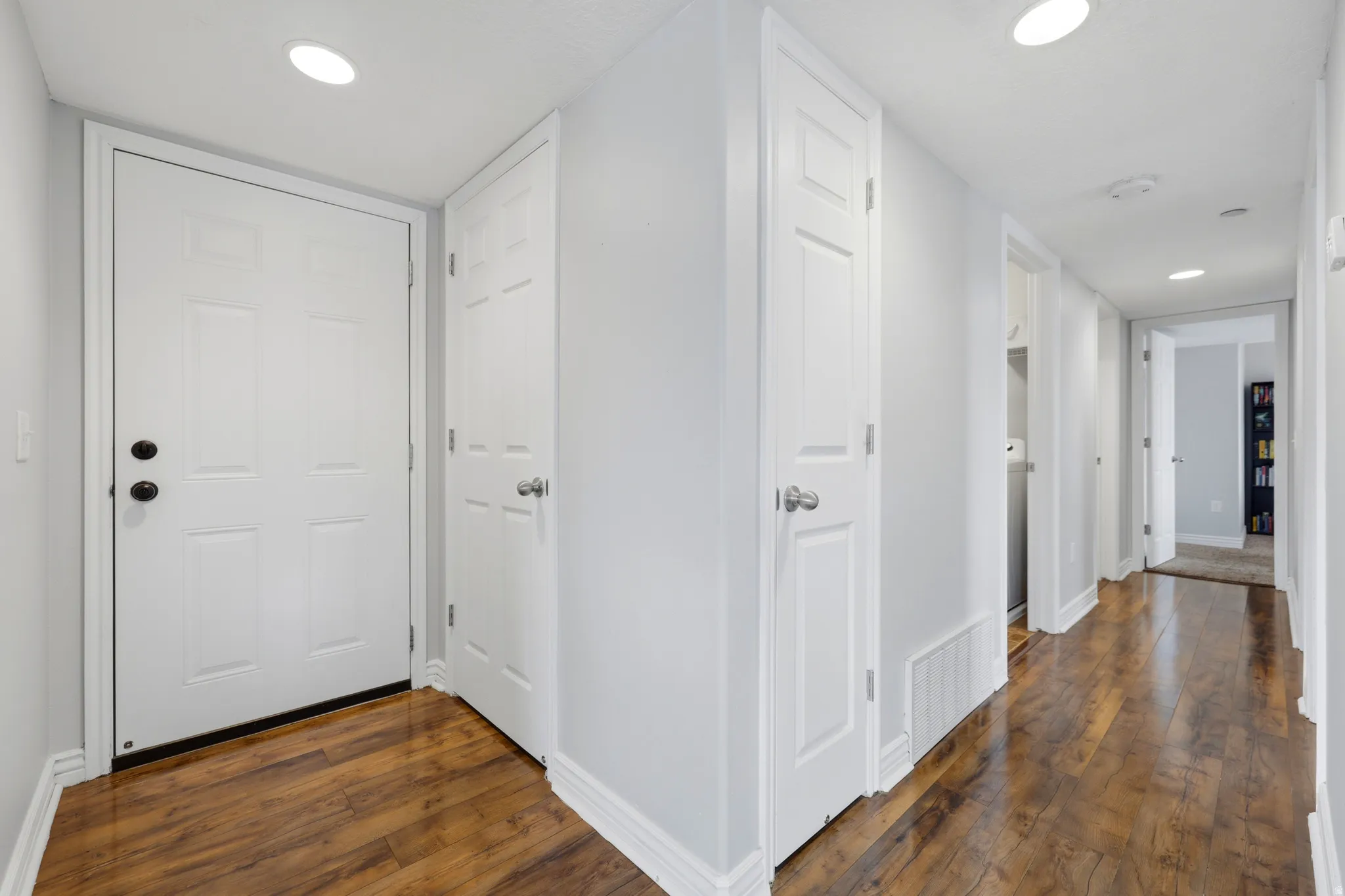 Entryway featuring a white paneled door with black hardware, wood-finish flooring, recessed lighting, and white baseboards