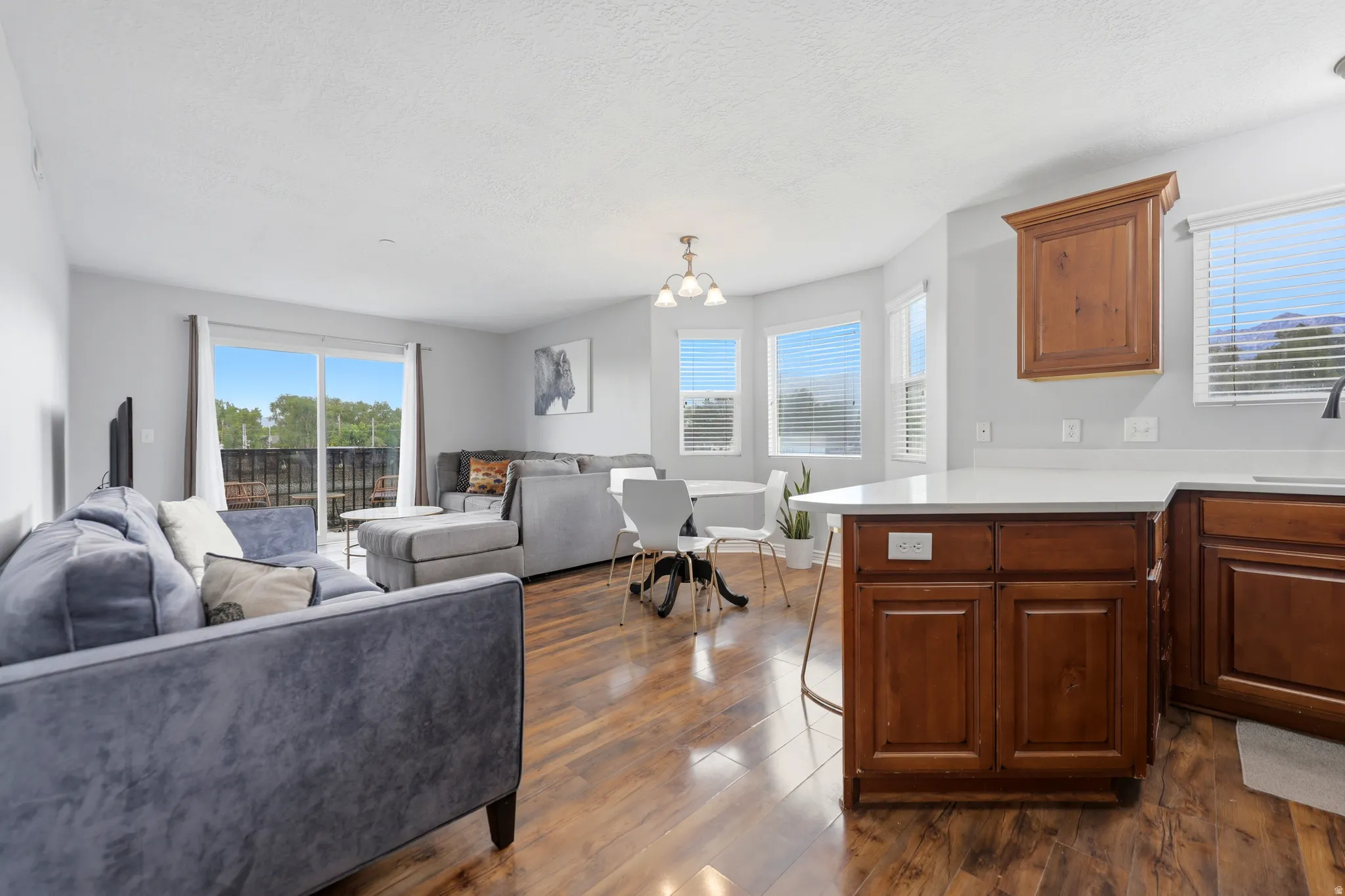 Open-concept living area featuring wood-finish flooring, a kitchen island with a white countertop, and a dining area with a bay window