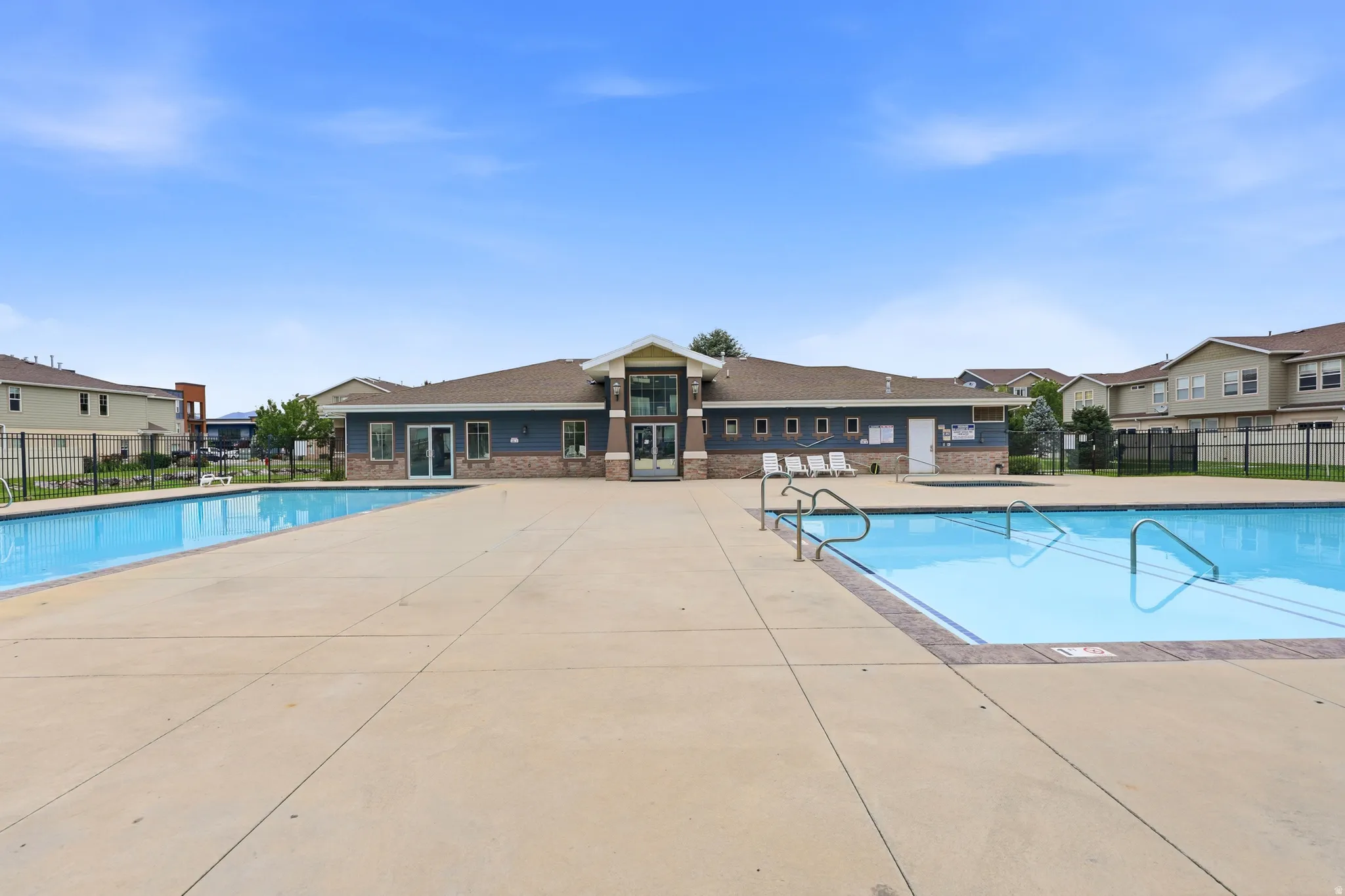 Community clubhouse featuring a brick and siding exterior, multiple swimming pools, and extensive concrete decking