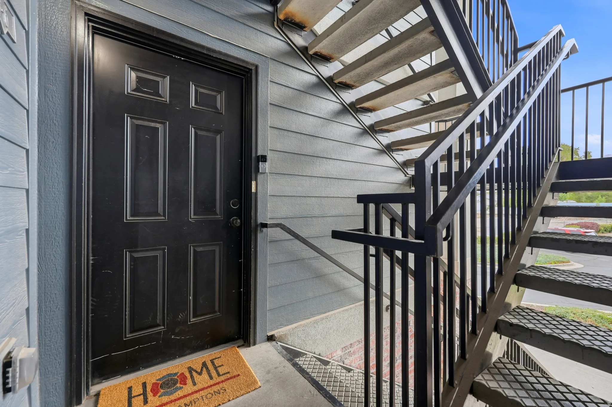 Exterior entry featuring a paneled black door, horizontal siding, concrete flooring, and an external metal staircase with matching railings