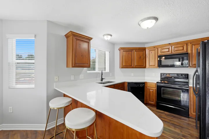 Kitchen featuring a peninsula with a white countertop, wood-finish cabinetry, black appliances, a double basin sink with a matte black faucet, and hard surface flooring
