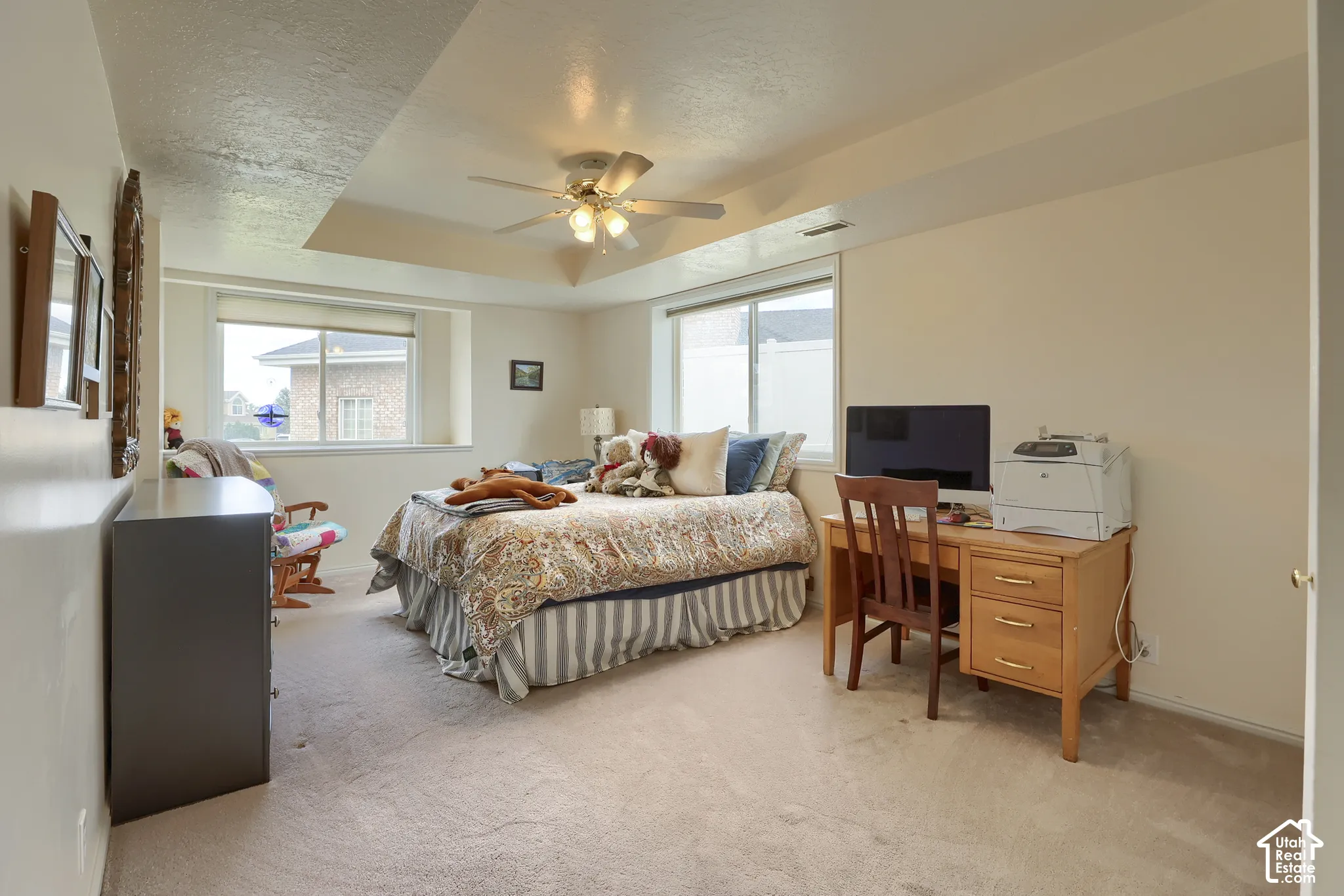 Bedroom featuring a tray ceiling with a ceiling fan, two large windows, carpet flooring, and neutral wall tones