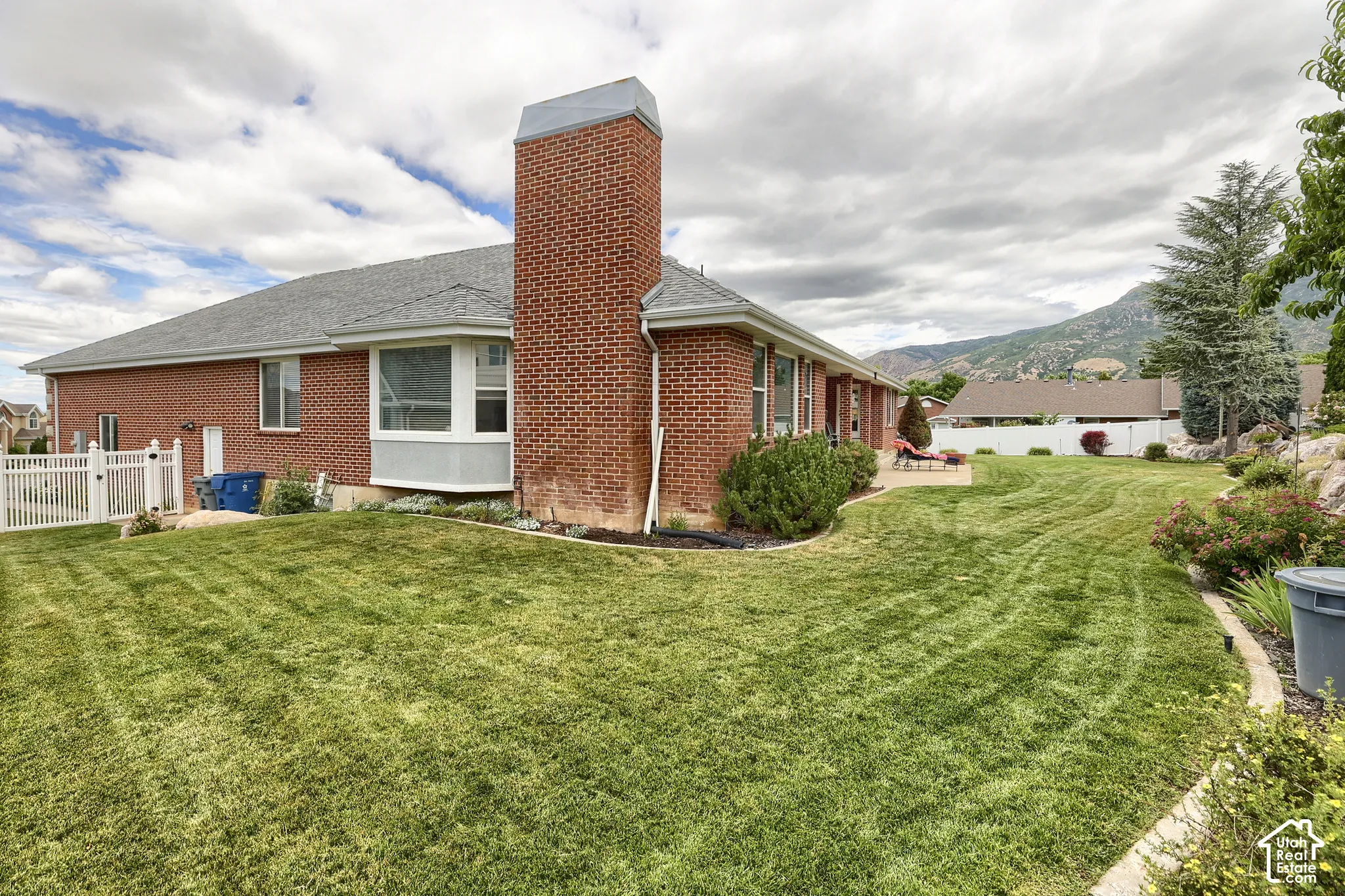 Expansive lawn area featuring a paved patio, red brick exterior, bay window, and surrounding landscaping