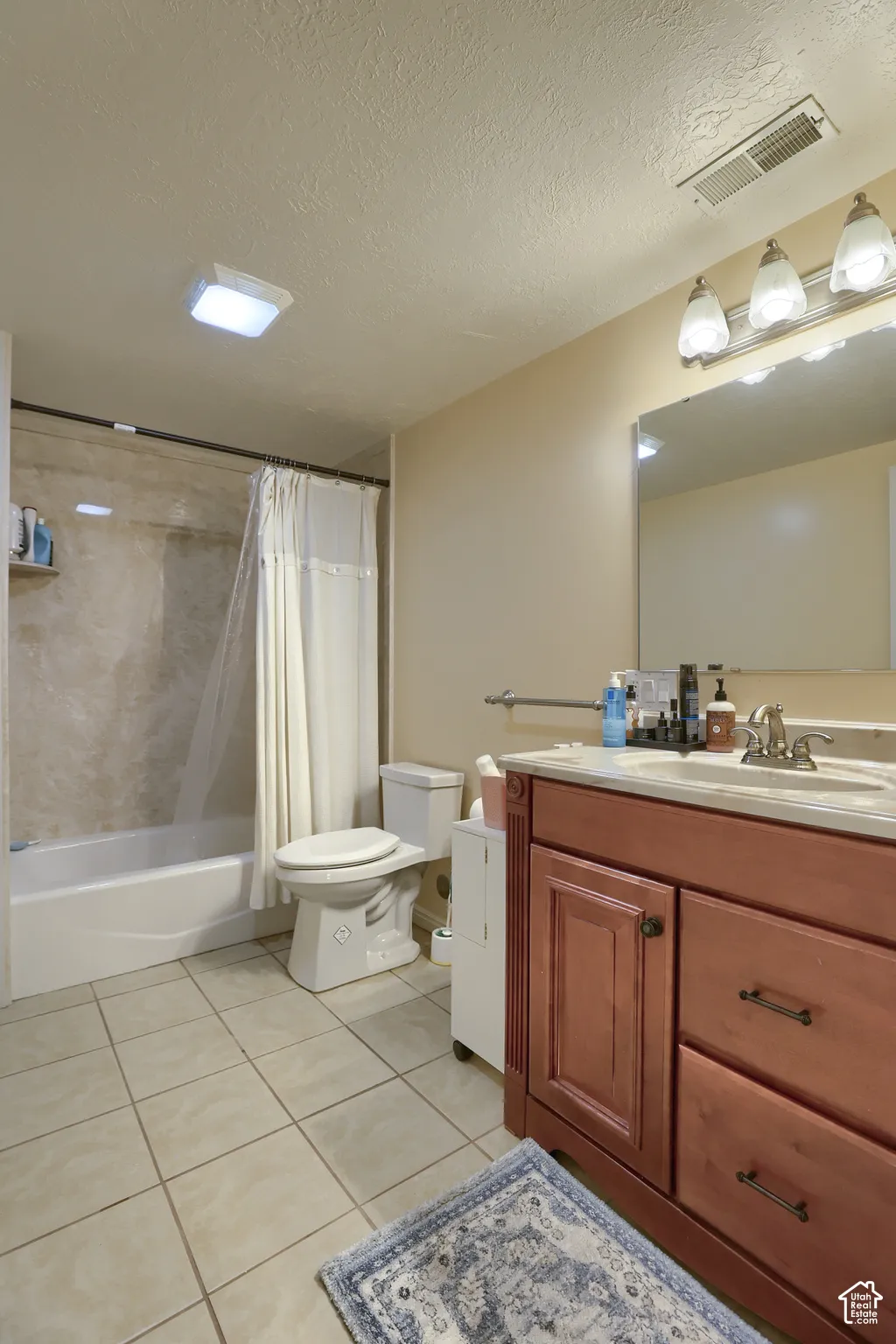Bathroom featuring a wood-finish vanity with a light-toned countertop, a shower-tub combination with a tiled surround, and large format floor tiling