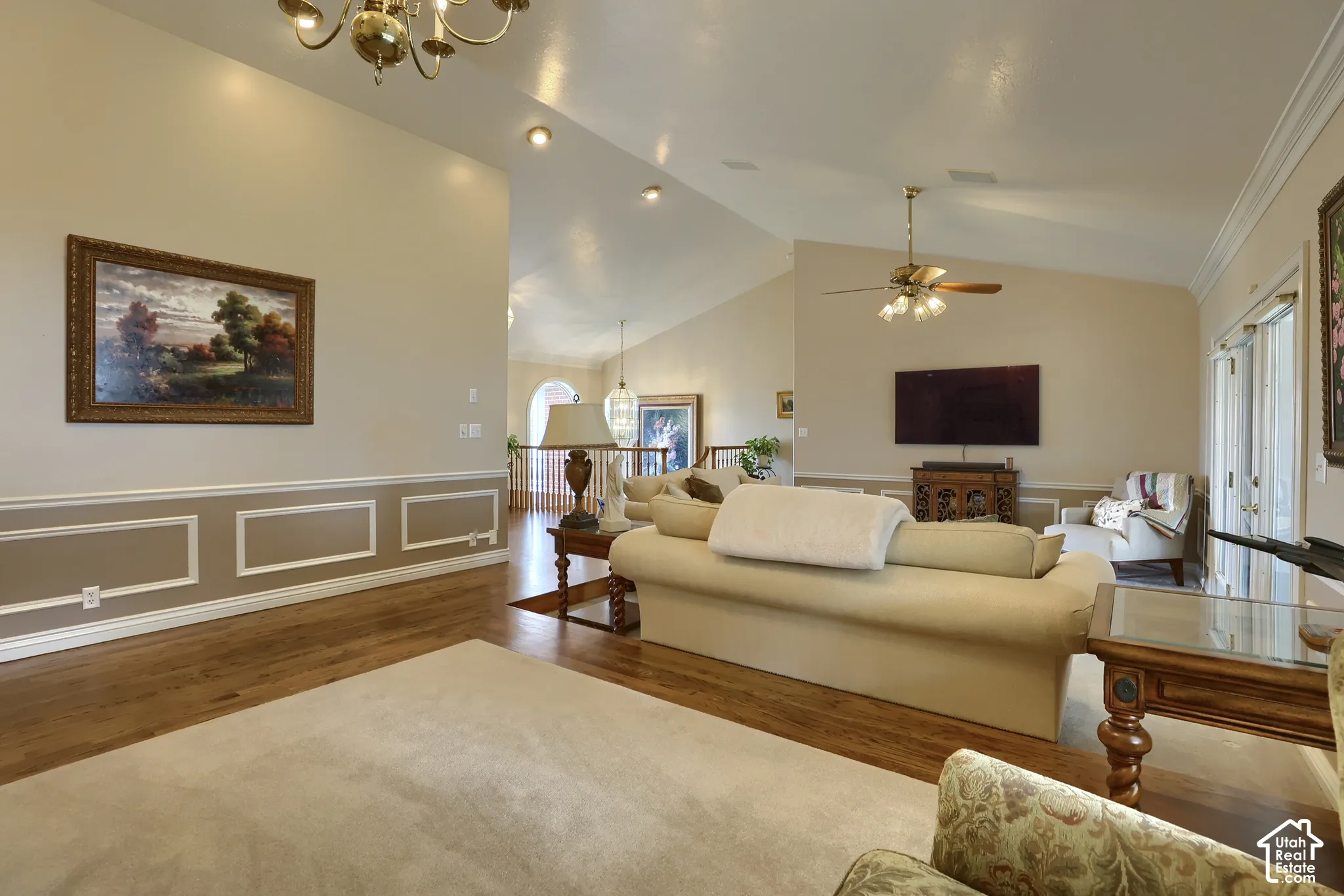 Living room featuring wood-finish flooring, vaulted ceilings, recessed lighting, and chair rail molding with decorative paneling