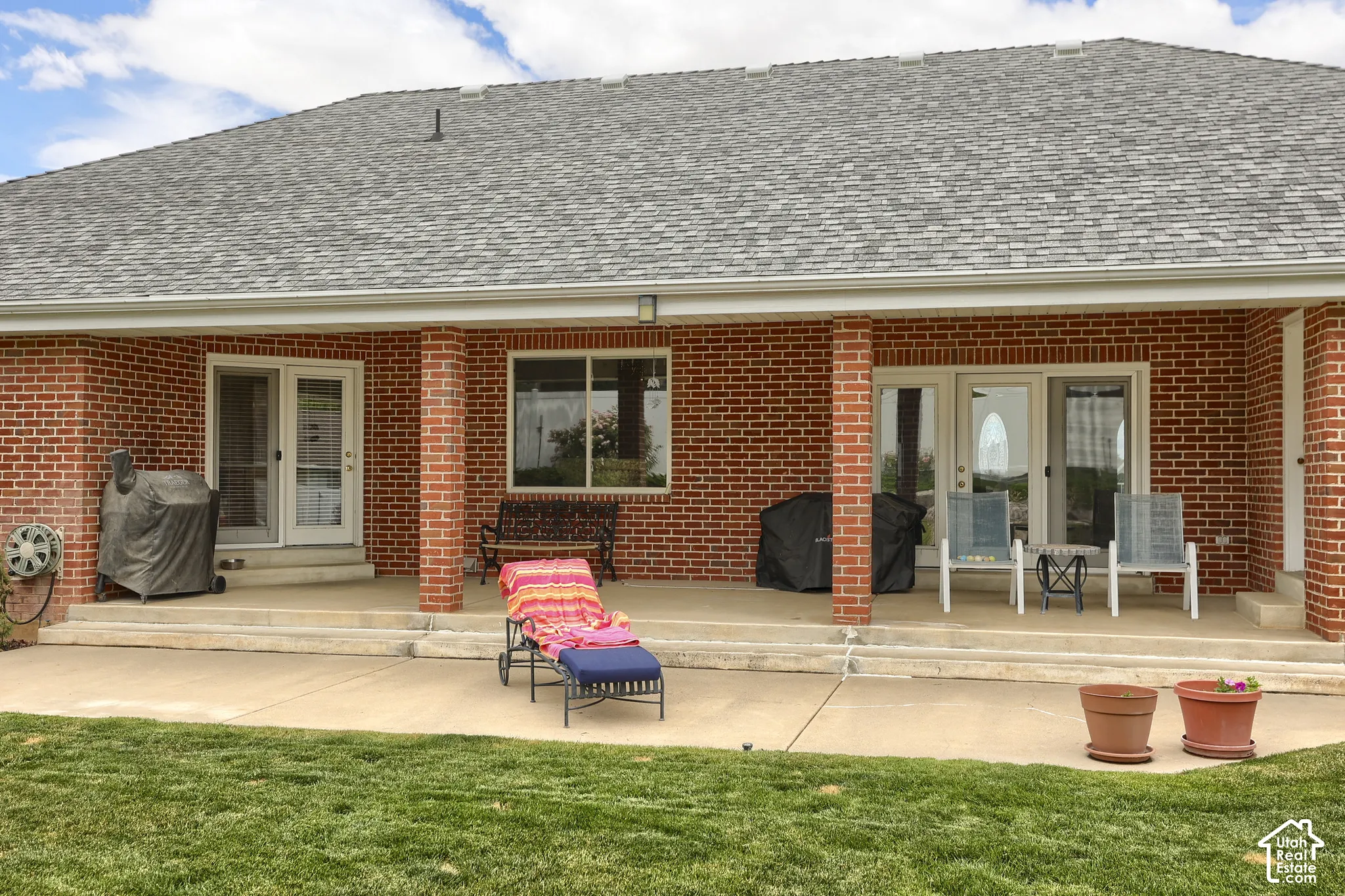 Covered patio featuring brick columns, red brick exterior, and a shingle roof