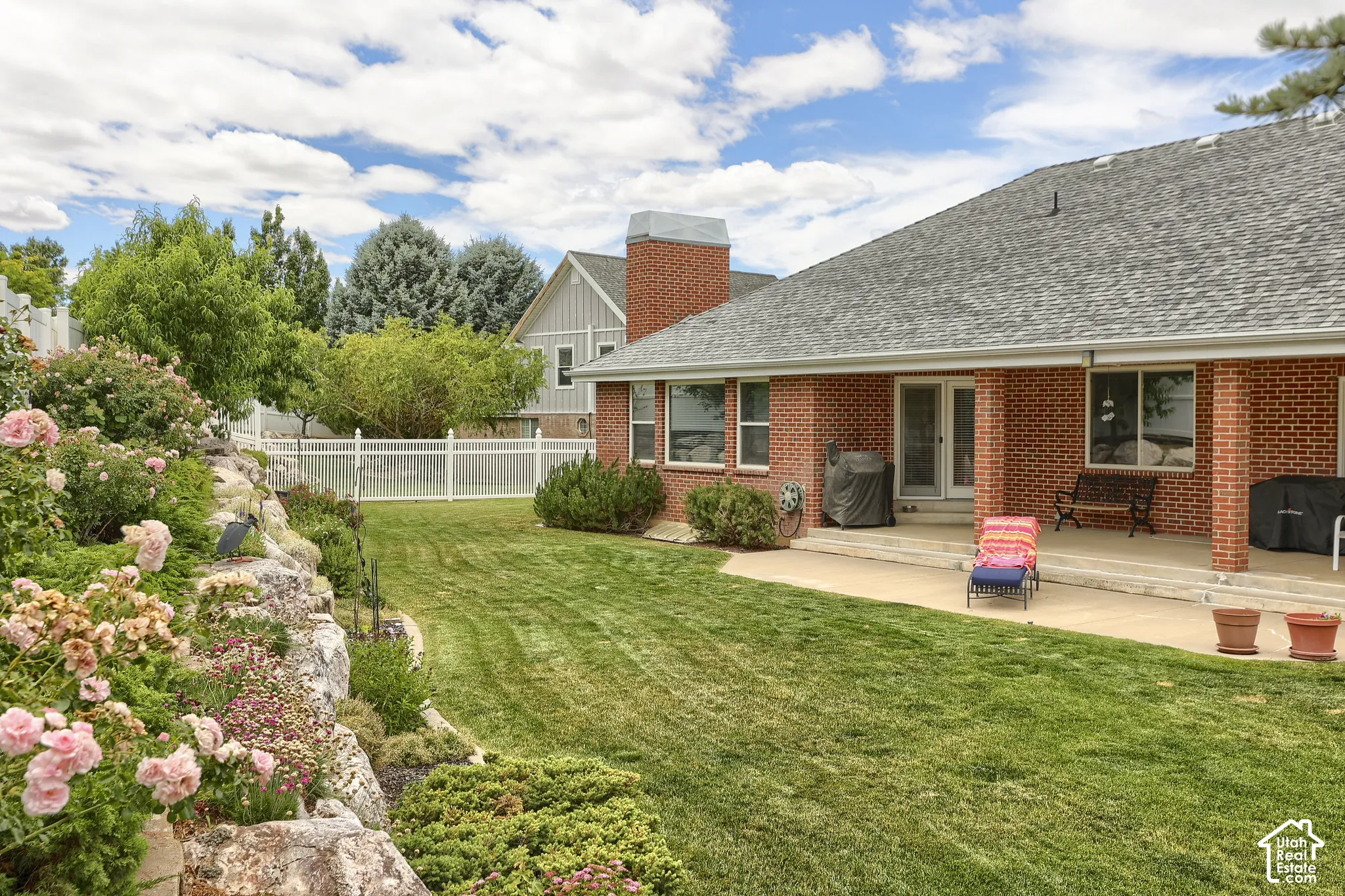 Expansive backyard featuring a manicured lawn, a rock garden with flowering shrubs, and a white picket fence
