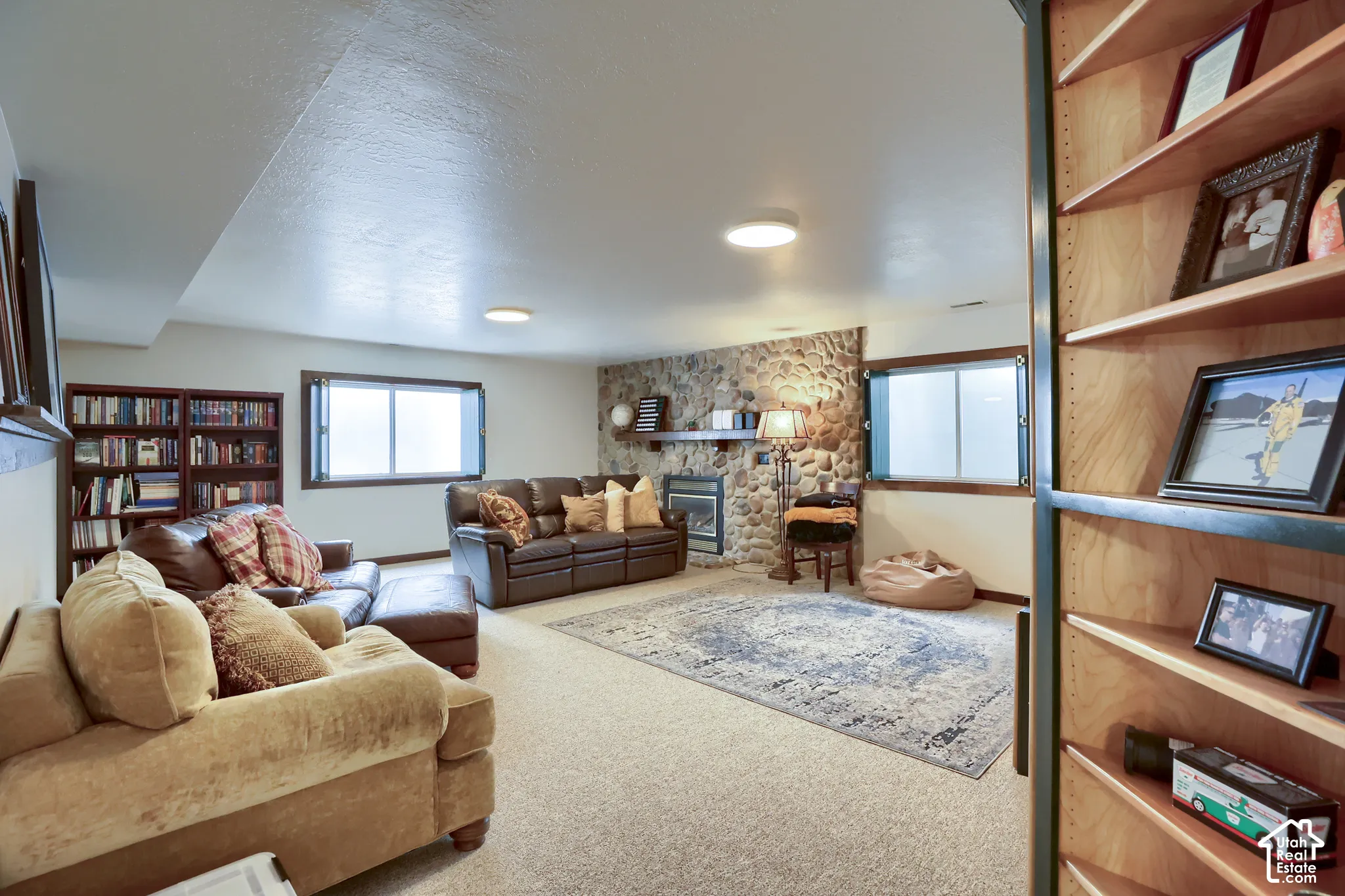 Spacious lower level featuring a stone-clad fireplace, built-in shelving, two egress windows, and recessed lighting