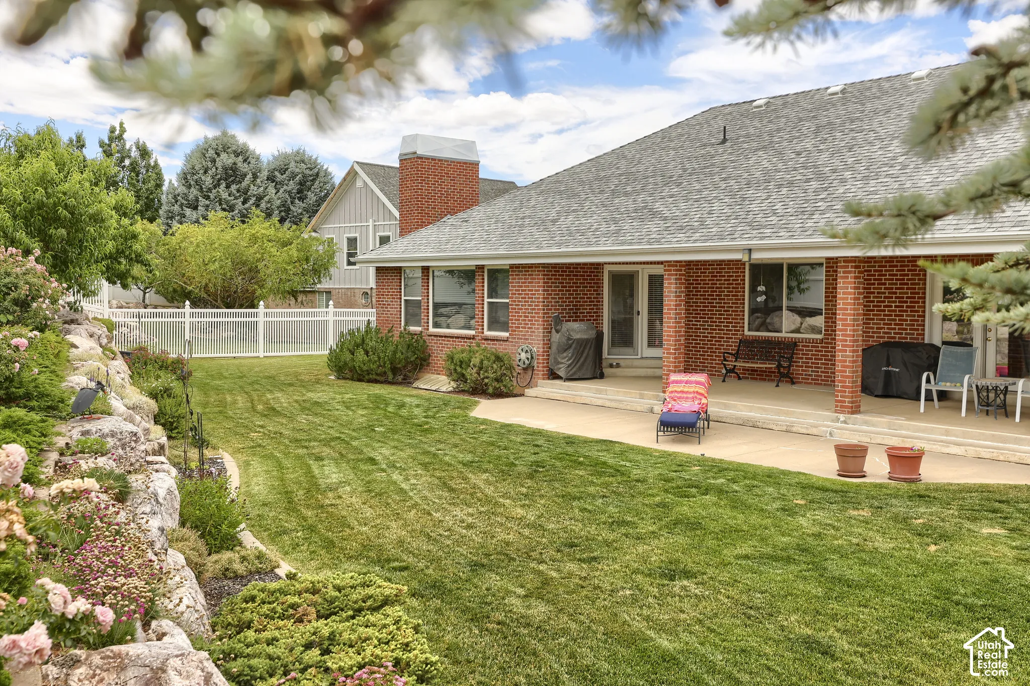 Expansive backyard featuring a manicured lawn, established rock landscaping with flowering shrubs, and a rear patio