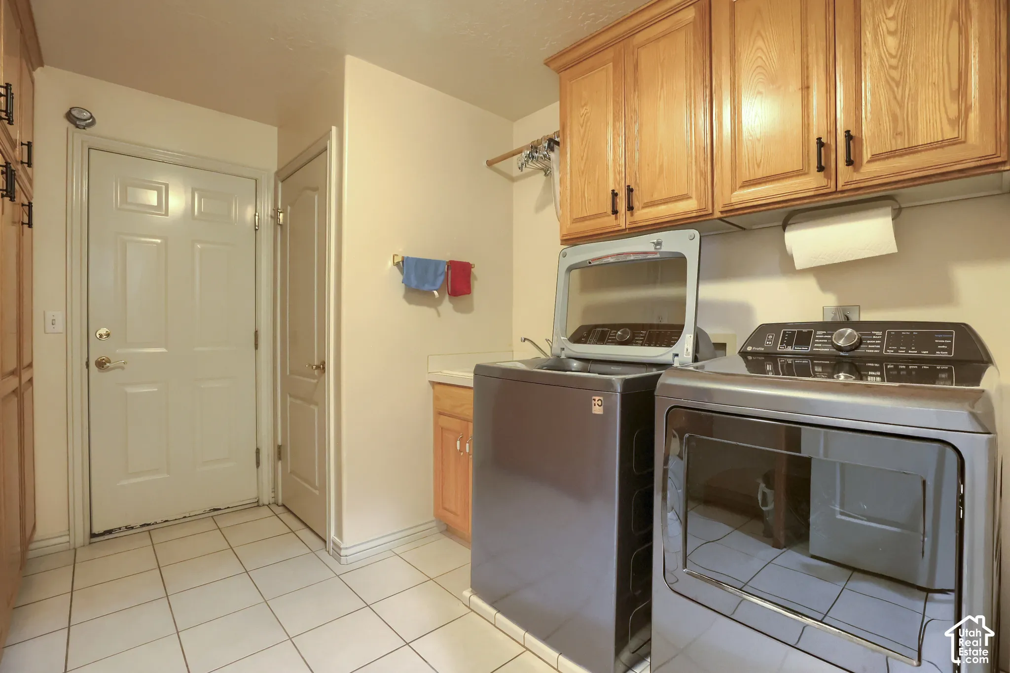 Laundry room featuring a white paneled door, tile flooring, and light wood cabinetry with dark hardware