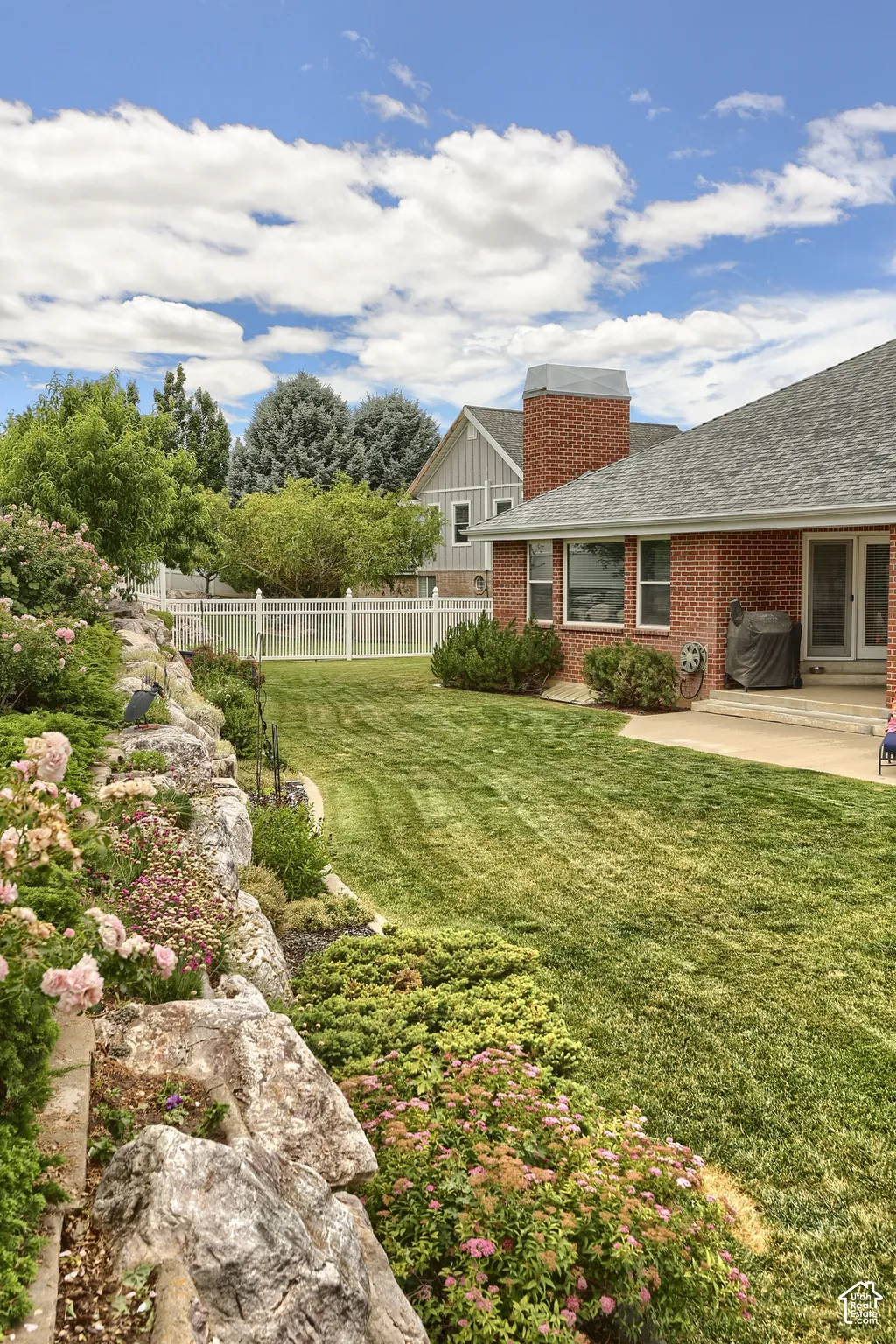 Spacious backyard featuring a manicured lawn, an expansive rock garden, and a white privacy fence