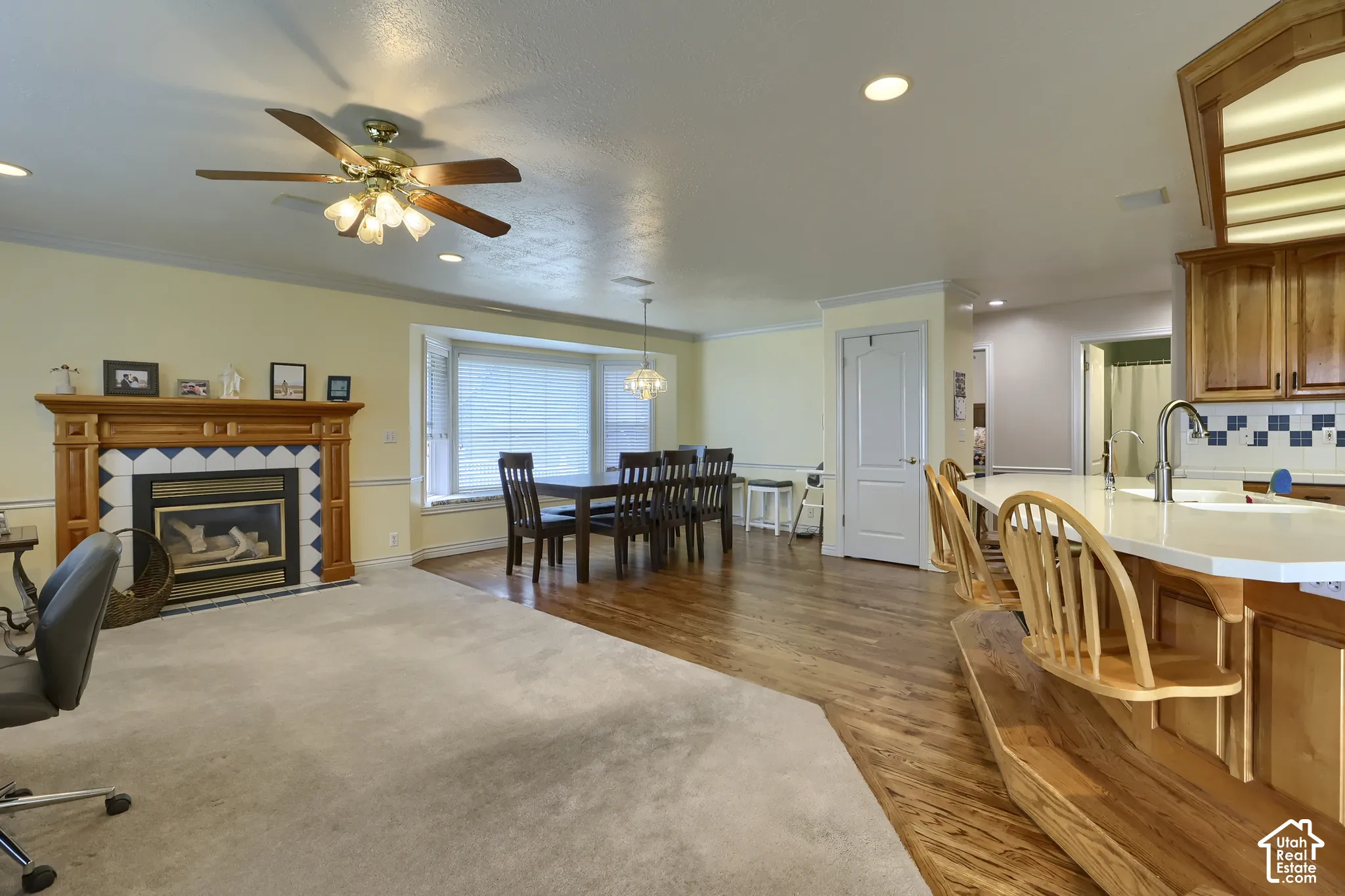Integrated living and dining space featuring a fireplace with a wood mantle and tile surround, a bay window, and a kitchen island with seating