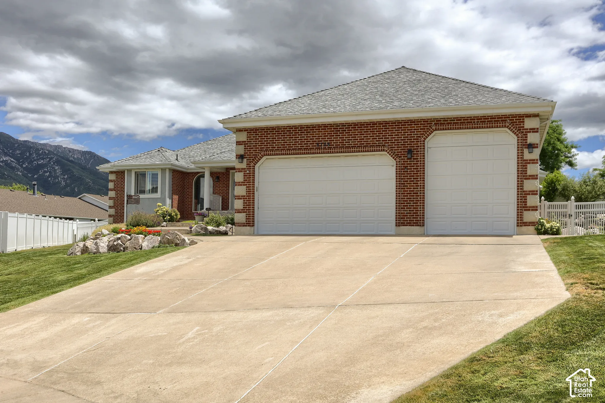 Brick exterior with a three-car garage, concrete driveway, and front landscaping featuring rockery and plantings