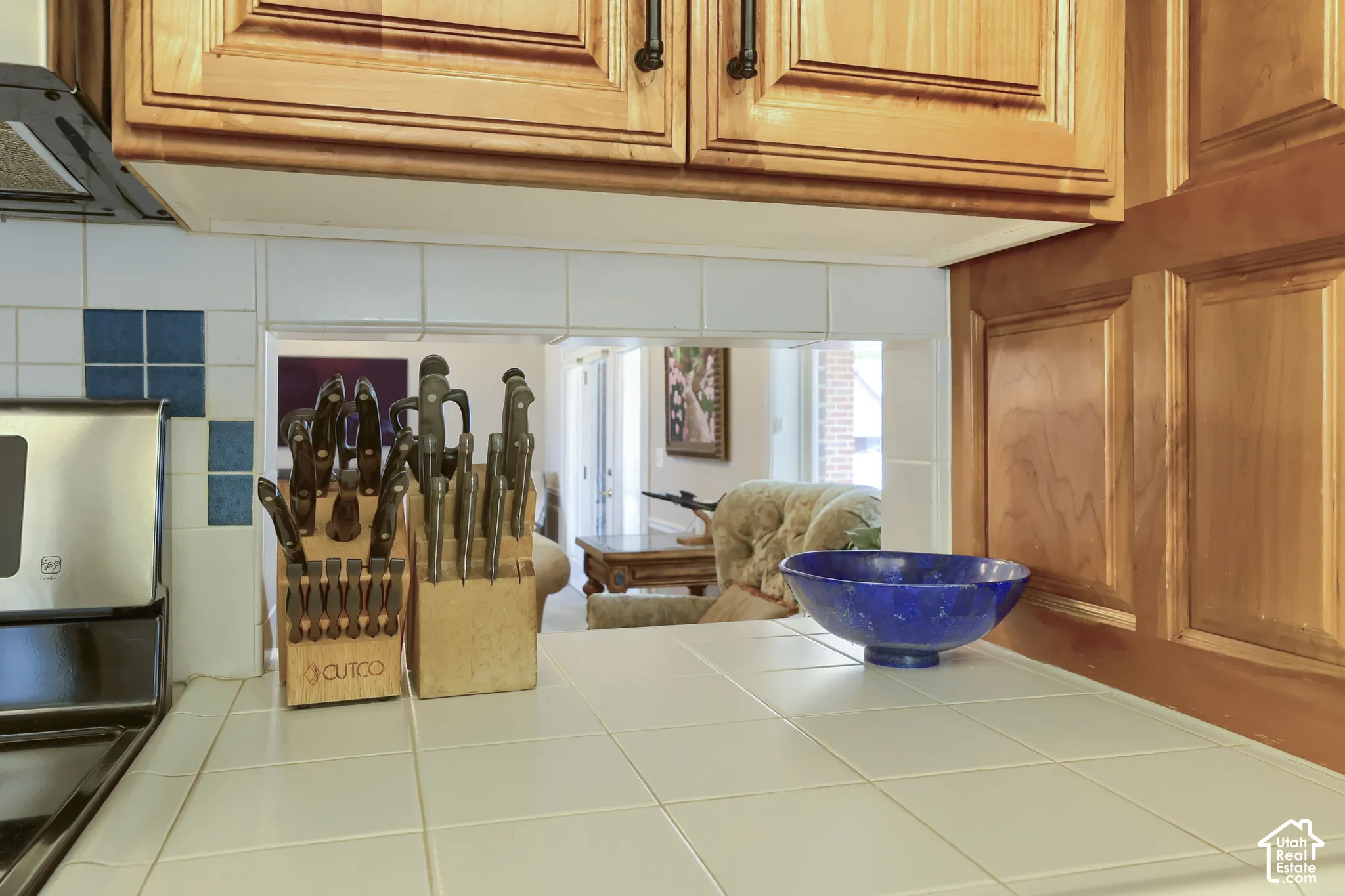 Kitchen featuring light wood cabinetry, white tile countertops, and a white tile backsplash with blue accents
