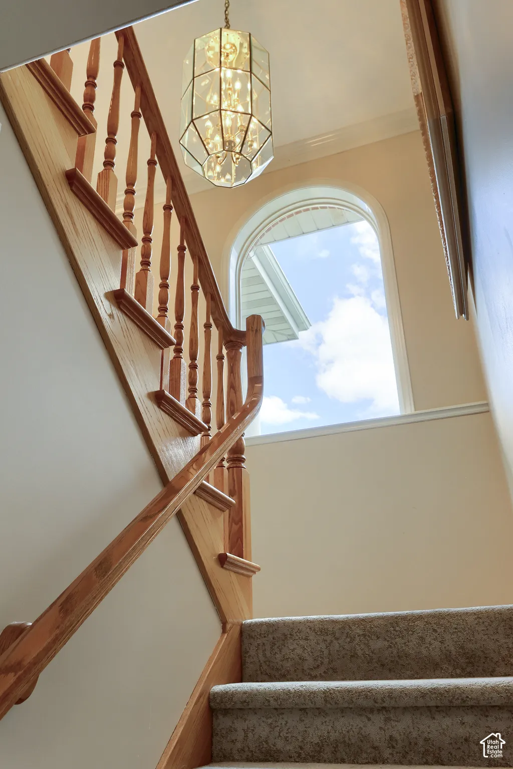 Carpeted staircase with light wood banister and spindles, illuminated by a decorative glass chandelier
