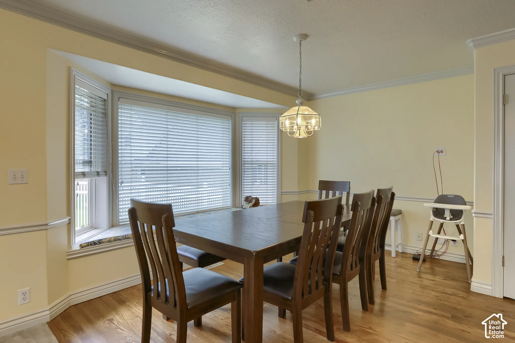 Dining area featuring a bay window, hardwood flooring, a ceiling-mounted chandelier, and crown molding