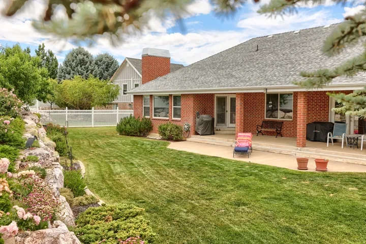 Expansive backyard featuring a manicured lawn, established rock landscaping with flowering shrubs, and a rear patio
